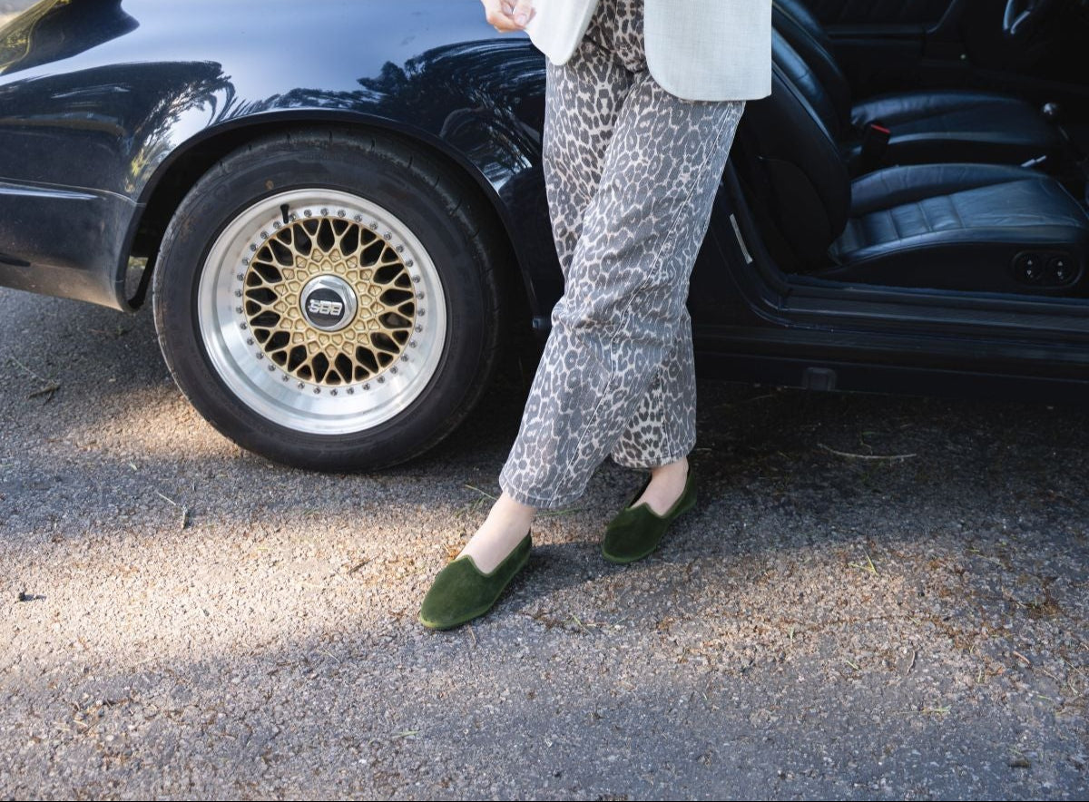 Woman standing next to a vintage car with trees in the background