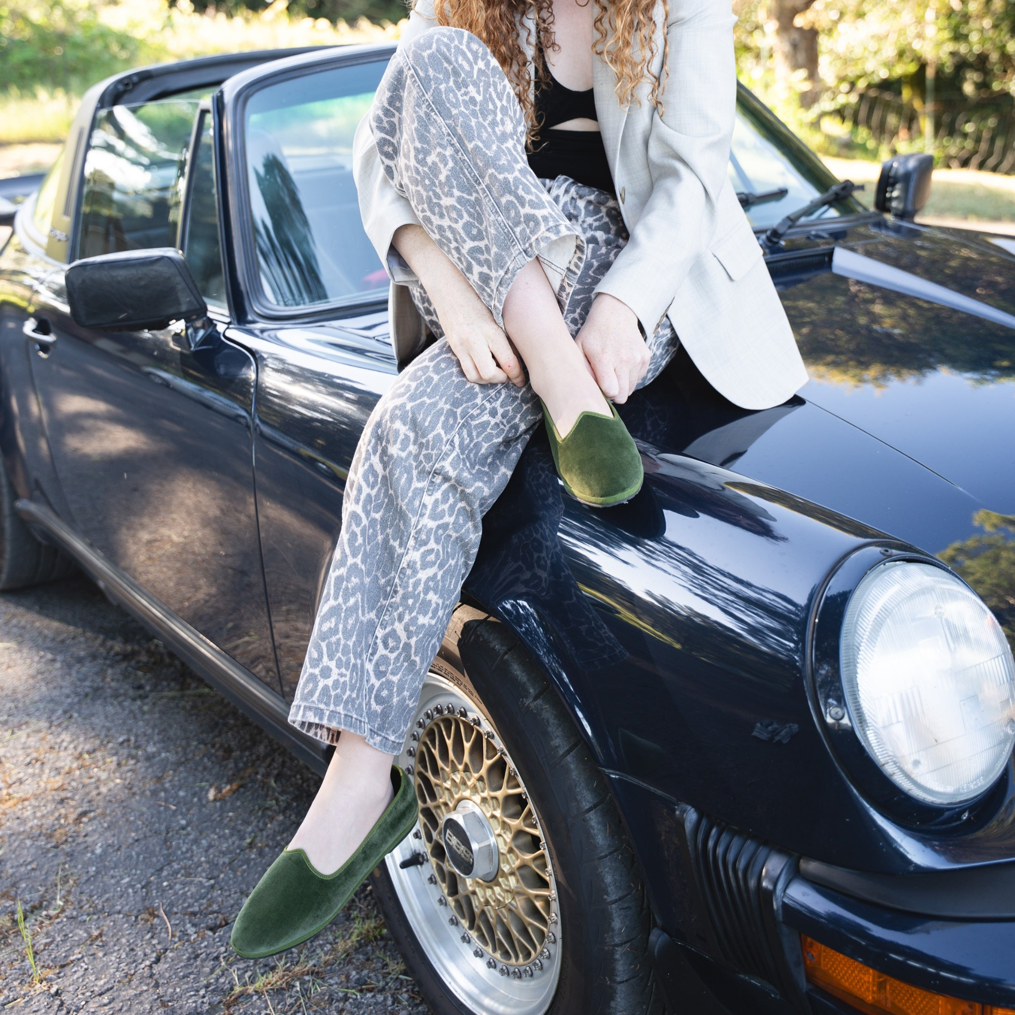 Woman sitting on a classic black car with trees in the background